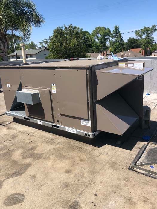 A beige, rectangular commercial HVAC unit sitting on a flat rooftop on a sunny day.