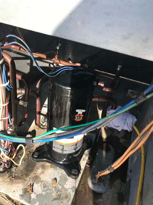 An outdoor air conditioning unit compressor, showing internal copper piping and wiring on a metal base.