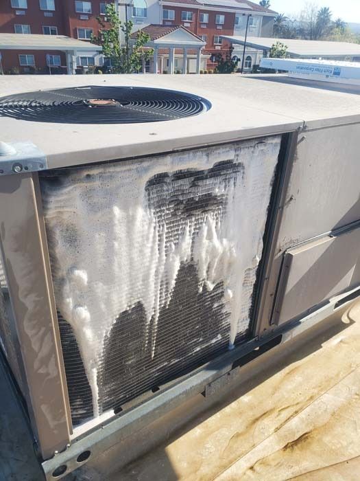 A rooftop HVAC unit with a large section of the cooling coils covered in thick white ice and frost.