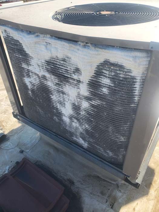 Outdoor air conditioning unit with metal coils covered in white frost or ice buildup, positioned on a roof surface.