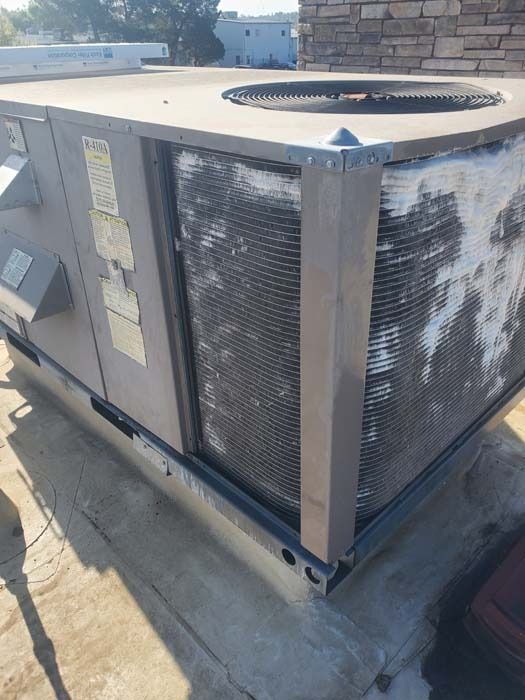 An exterior view of a rooftop HVAC unit with a large, rectangular condenser coil covered in white, dusty debris.