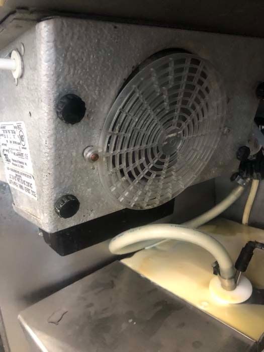 A mechanical refrigeration unit with a circular plastic fan cover, showing industrial tubing and part of a metal basin.