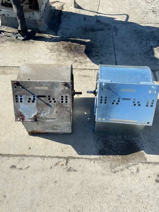 An old, rusted HVAC blower wheel positioned next to its new, clean, silver-colored replacement on a concrete surface.