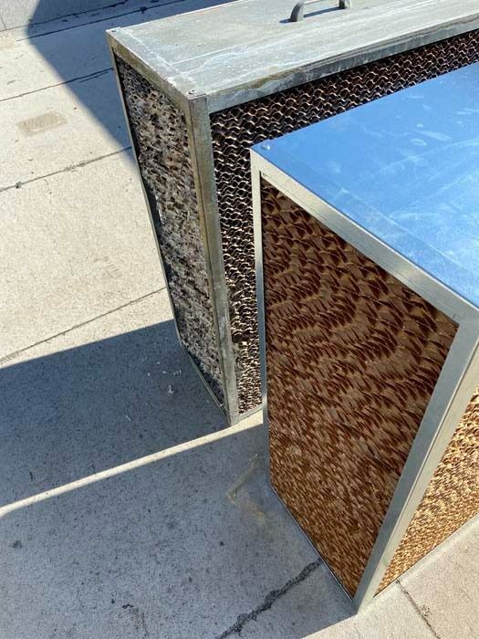 Two evaporative cooler pads, one old and discolored and one new, standing on concrete.