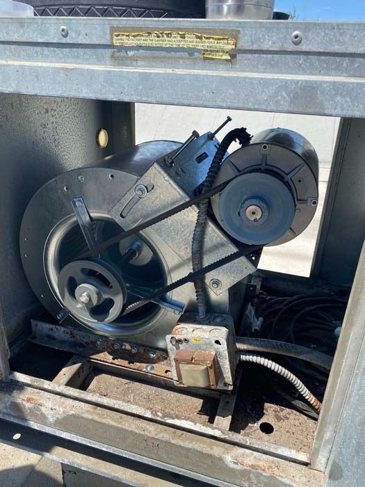 A belt-driven HVAC blower motor assembly with a metal fan housing and electrical components mounted in a steel cabinet.