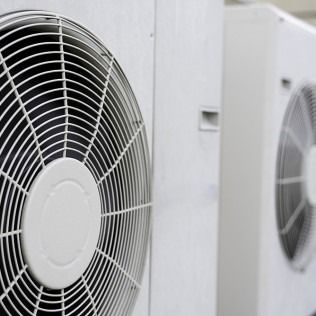 Two large, white industrial air conditioning units with circular wire fan guards side-by-side.