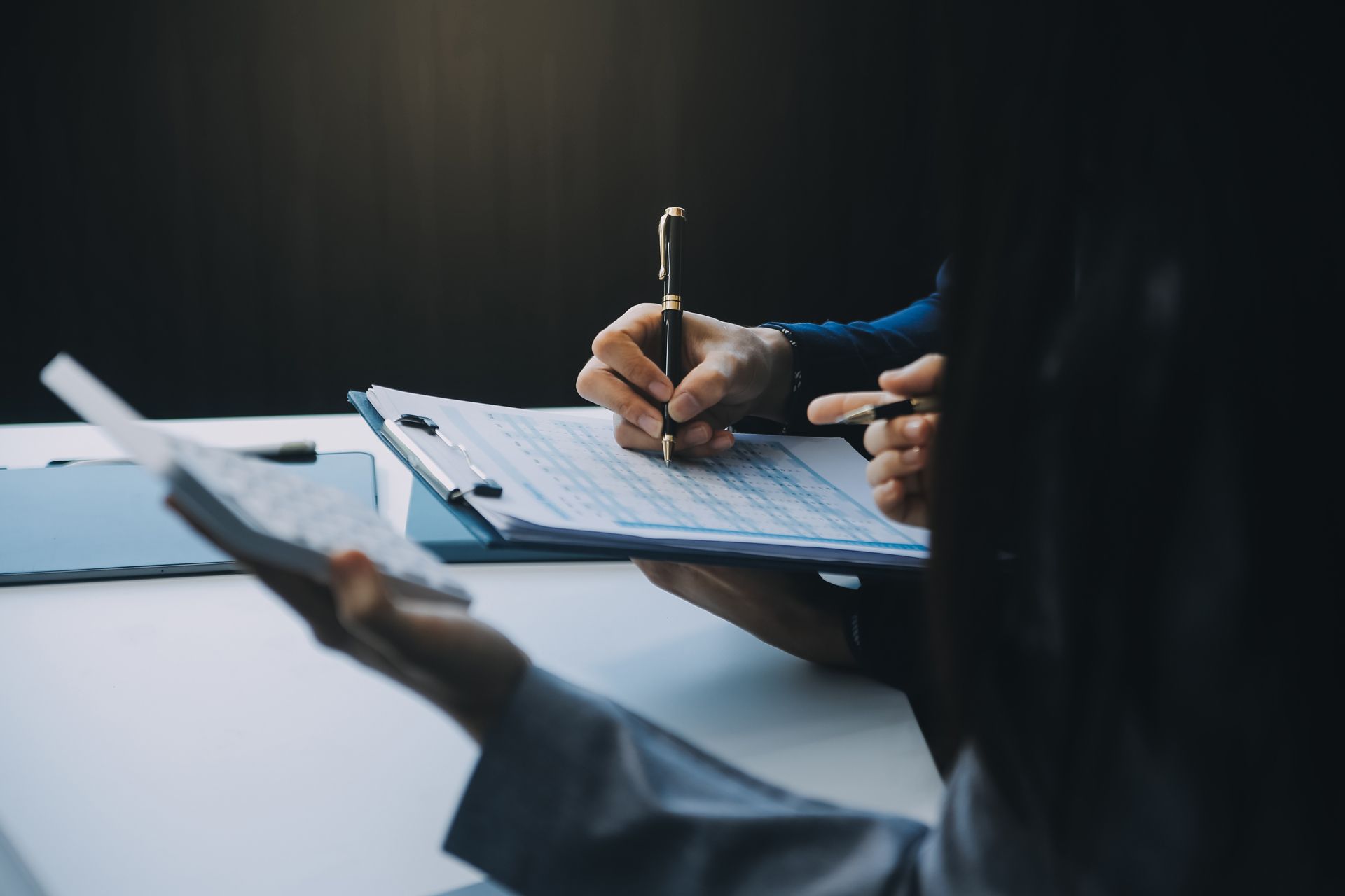 Hands writing on a clipboard during a meeting at a table