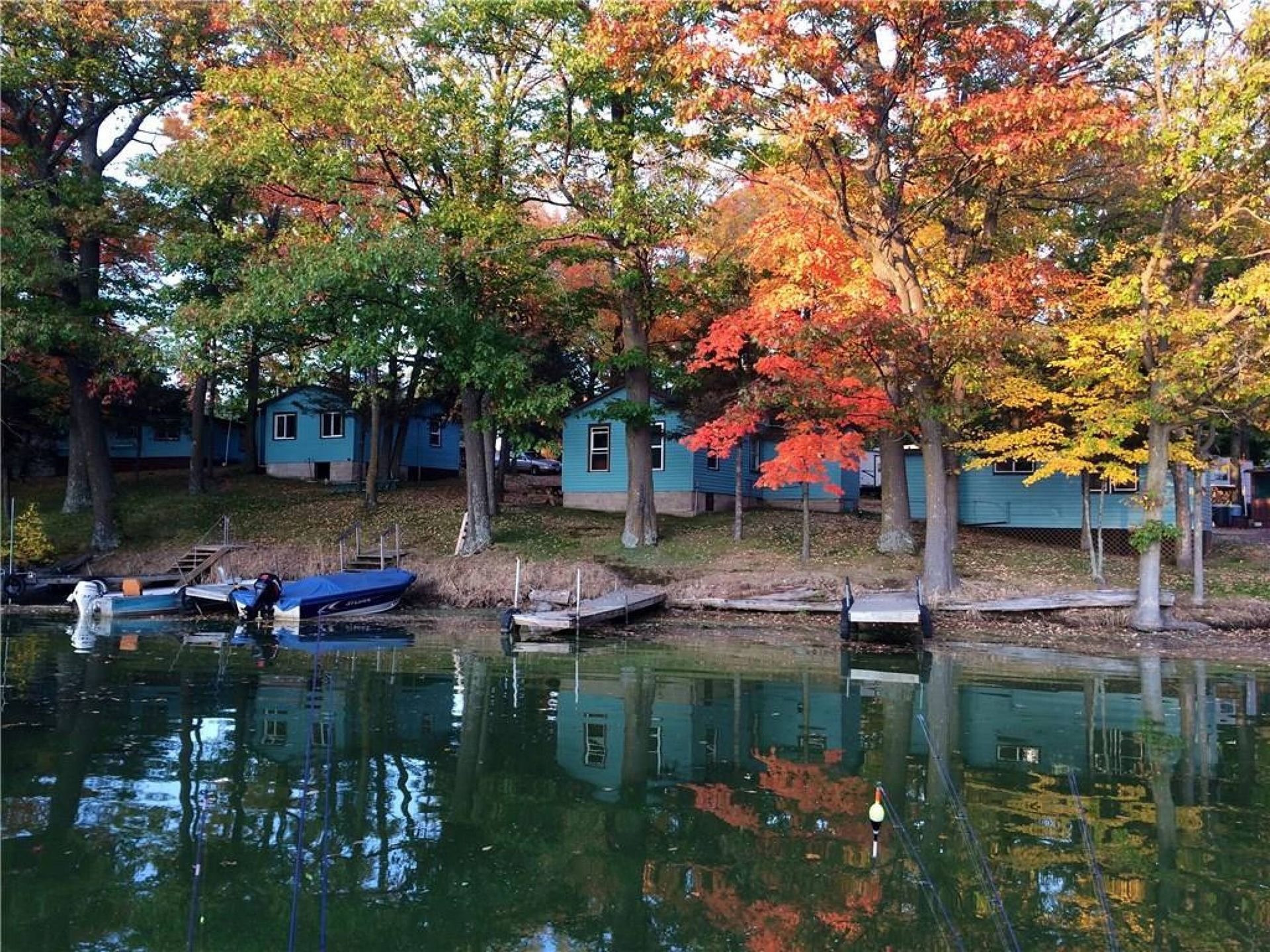 Autumn trees reflecting in a calm pond beside small lakeside cabins and docks.