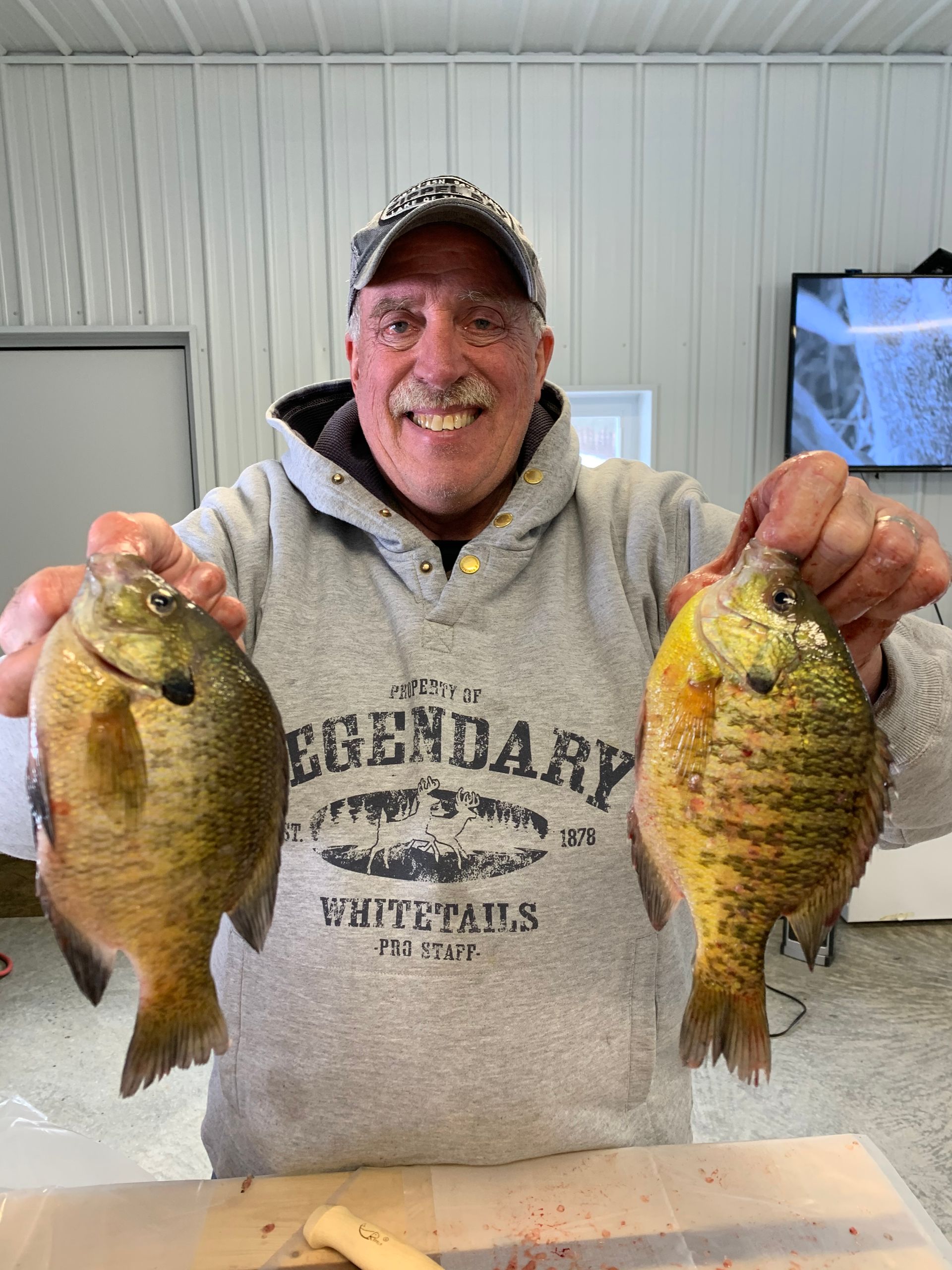 Man holding two fish indoors, smiling at the camera.