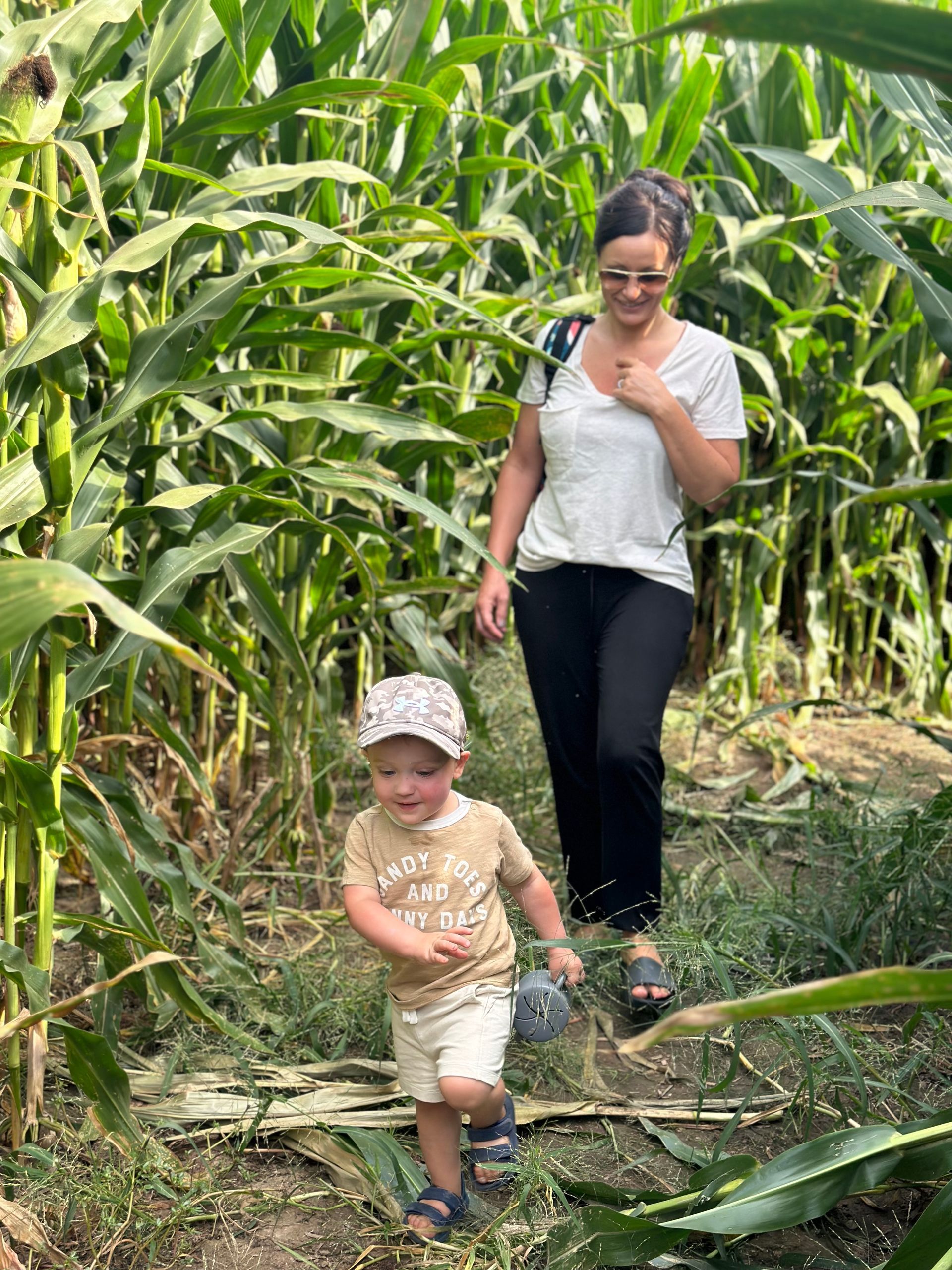 Woman and young child walking through a cornfield, surrounded by tall green plants.