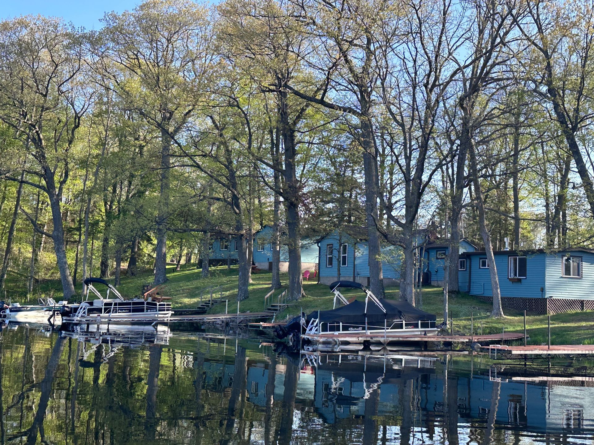 Lakeside cabin with picnic table, dock, and trees by a calm lake at sunset