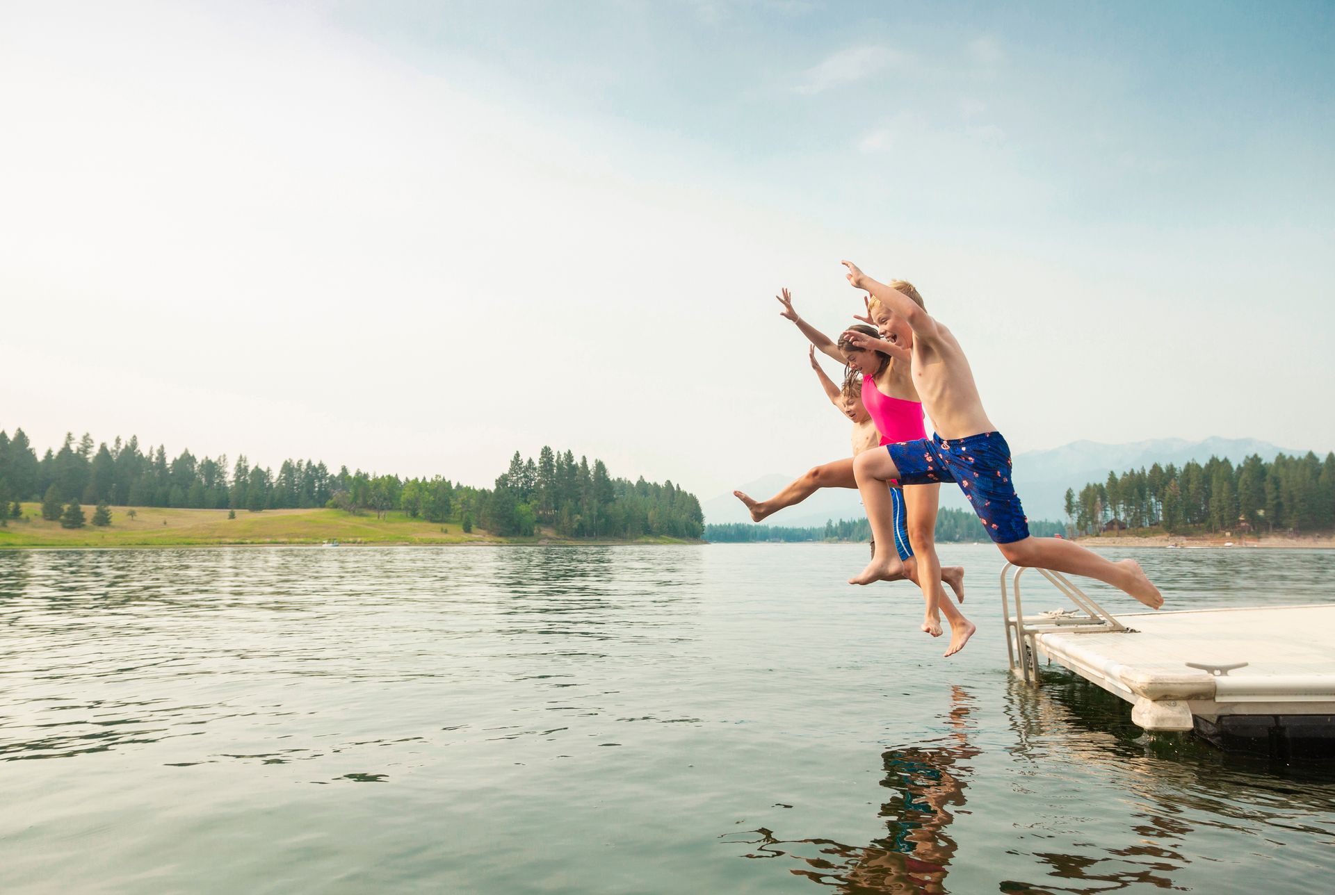 Two people leap from a dock into a calm lake on a sunny day