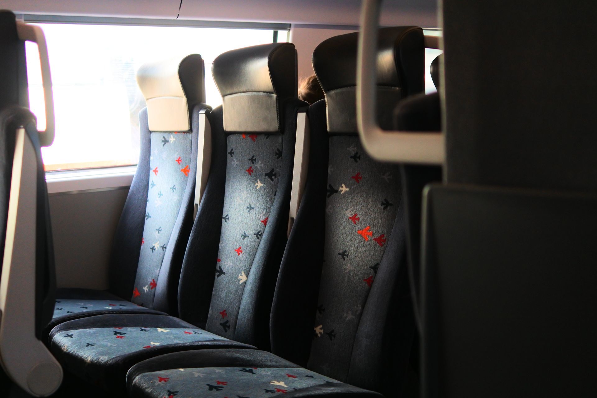 Empty train seats with blue patterned upholstery by a bright window