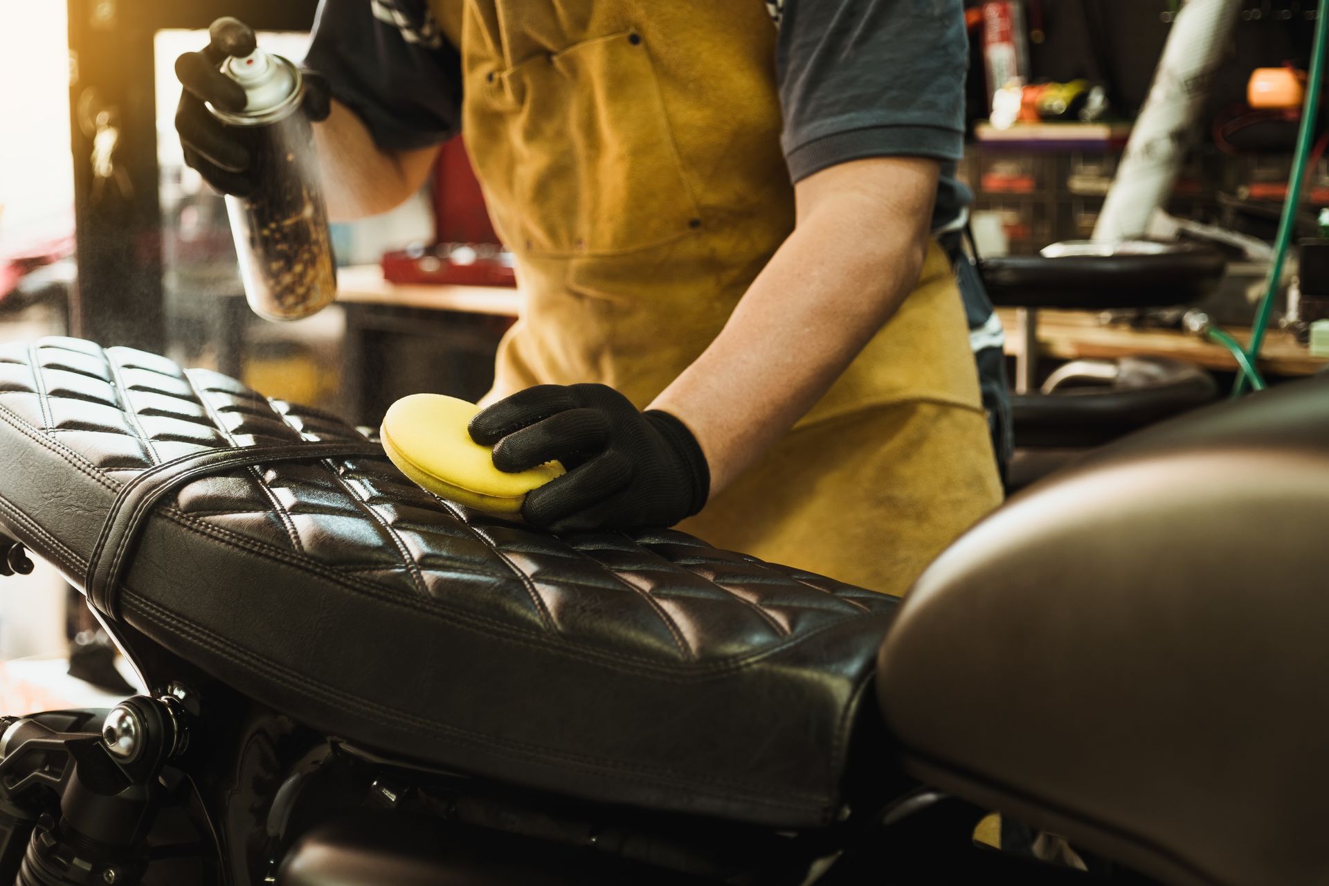 Person cleaning a black motorcycle seat with a sponge in a workshop