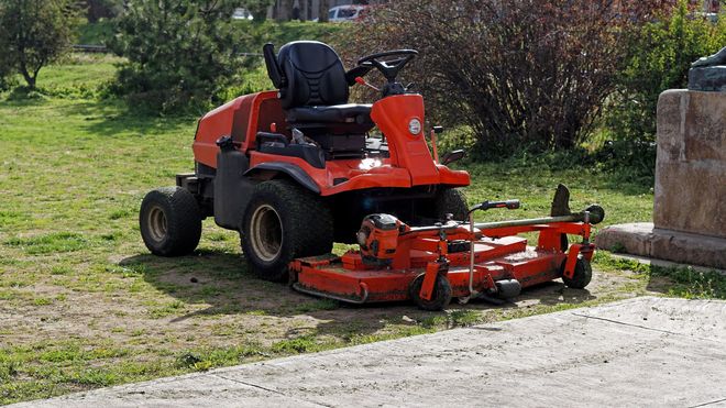 Red riding lawn mower parked on grass beside a stone wall and paved path