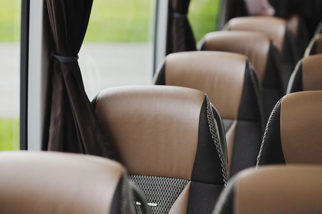 Empty bus seats with tan headrests and dark curtains by the windows
