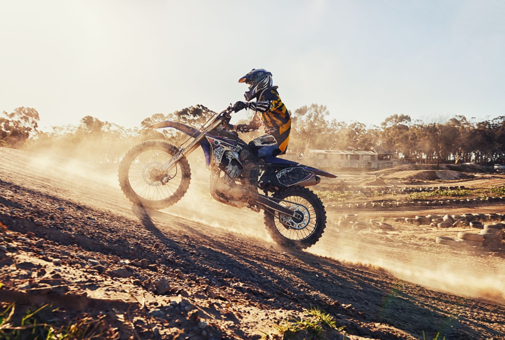 Motorcyclist riding uphill on a dusty dirt track, kicking up dust in warm sunlight