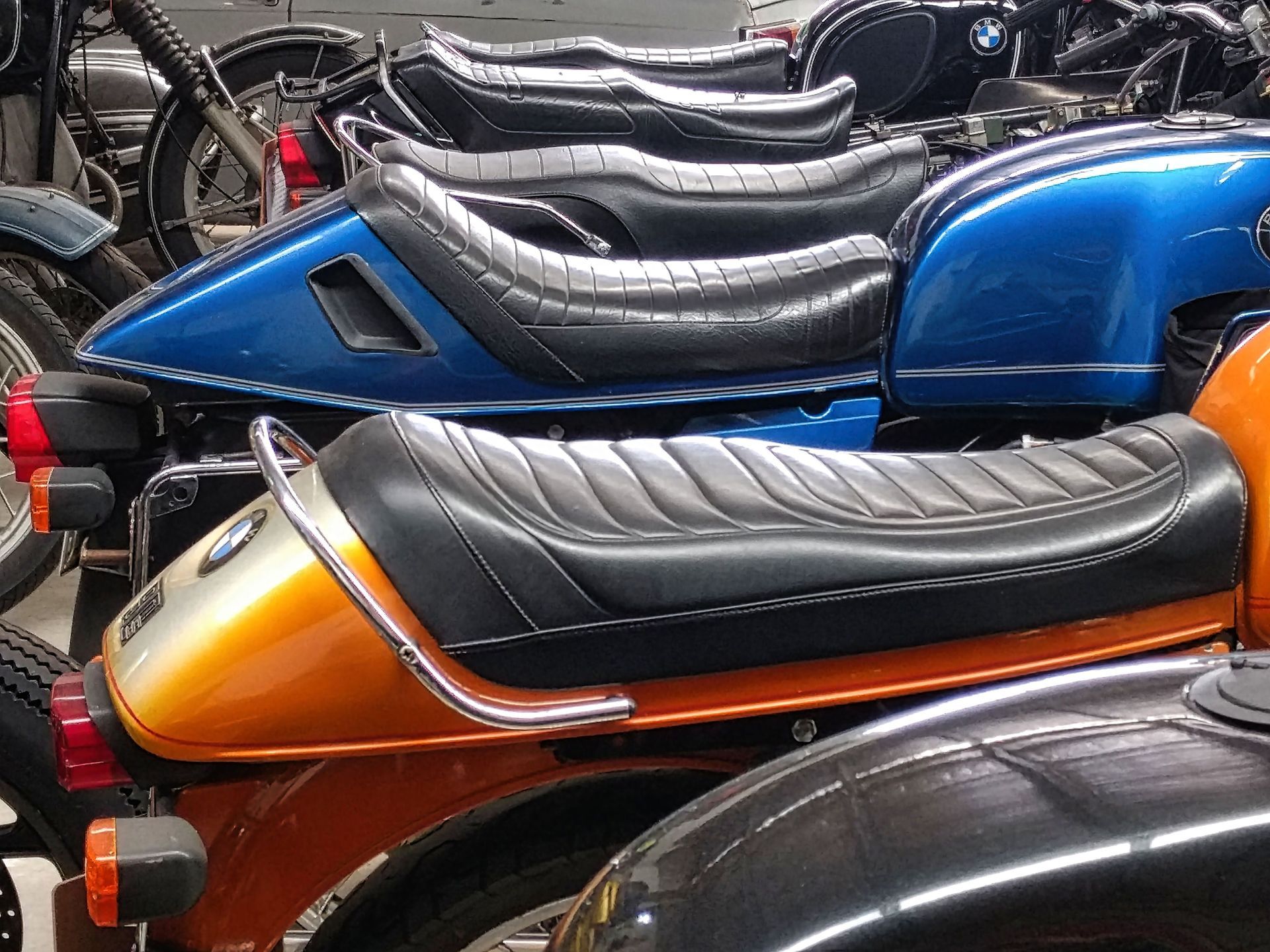 Row of parked motorcycles with colorful seats and fuel tanks, including blue, orange, and black bikes.