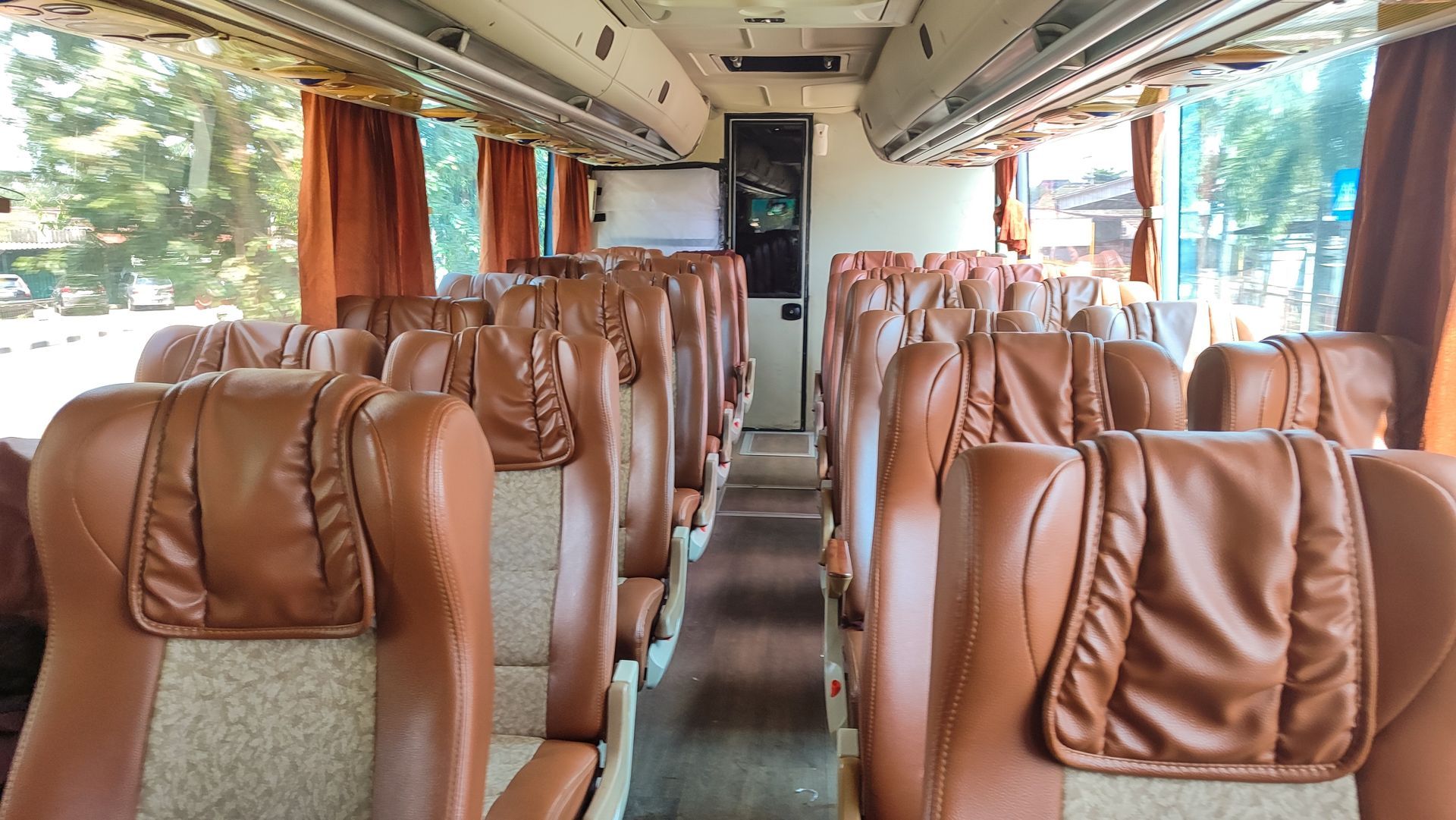 Empty bus interior with tan leather seats and orange curtains along the windows