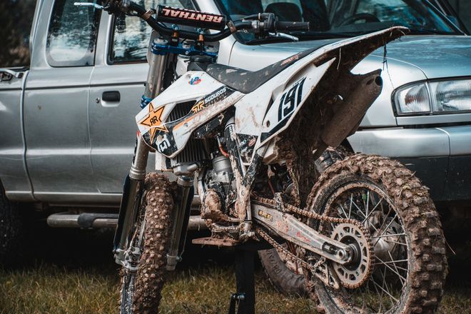 Mud-covered dirt bike parked in front of a silver pickup truck after a ride