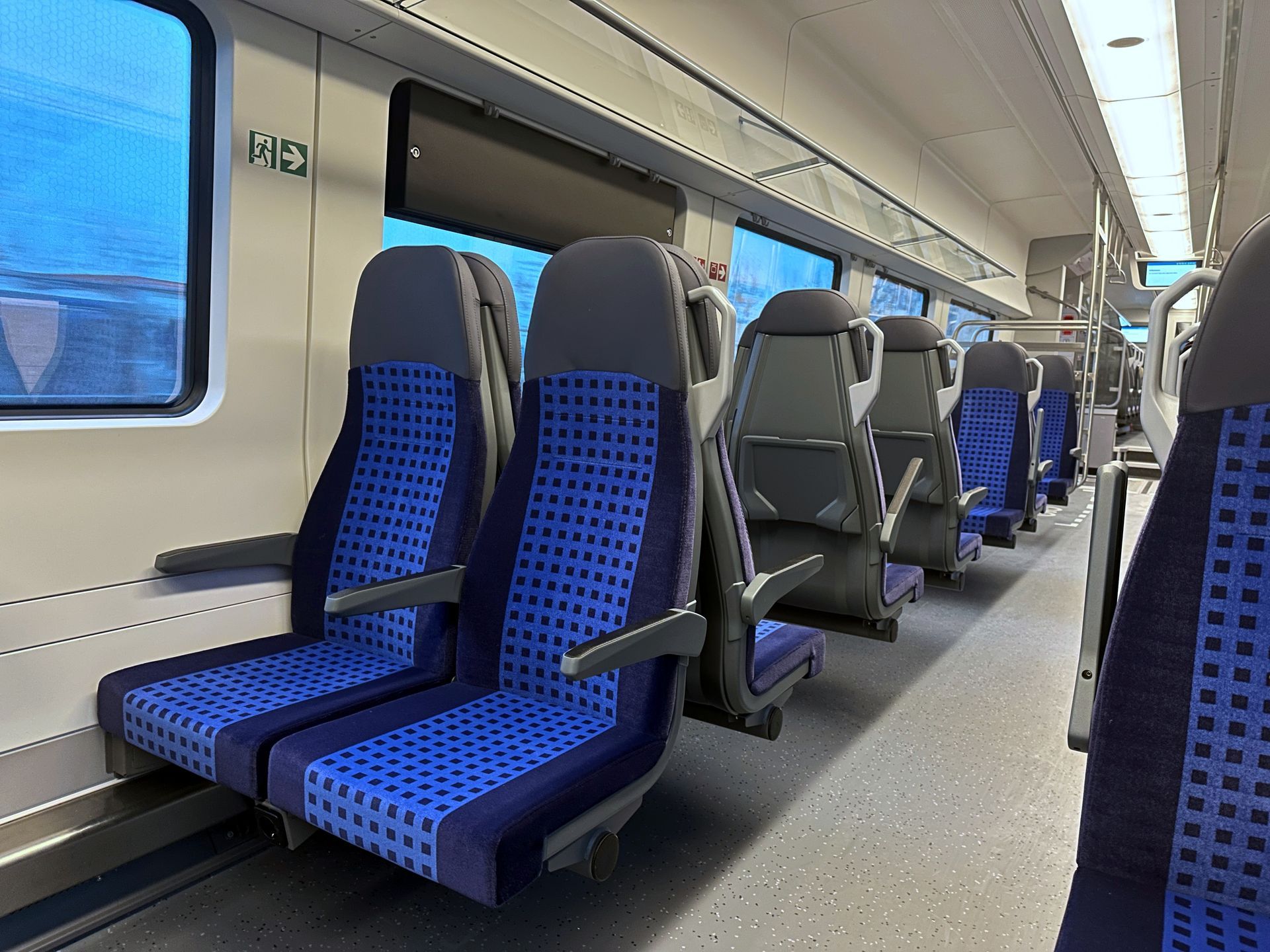 Inside a train carriage, rows of empty blue patterned seats line the aisle.