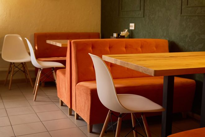 Empty cafe seating with orange booths, wooden tables, and white chairs on a tiled floor