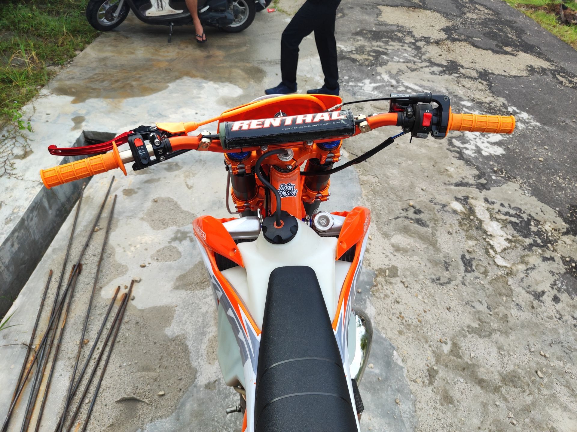 Orange dirt bike viewed from above on a concrete path, with handlebars and seat visible.