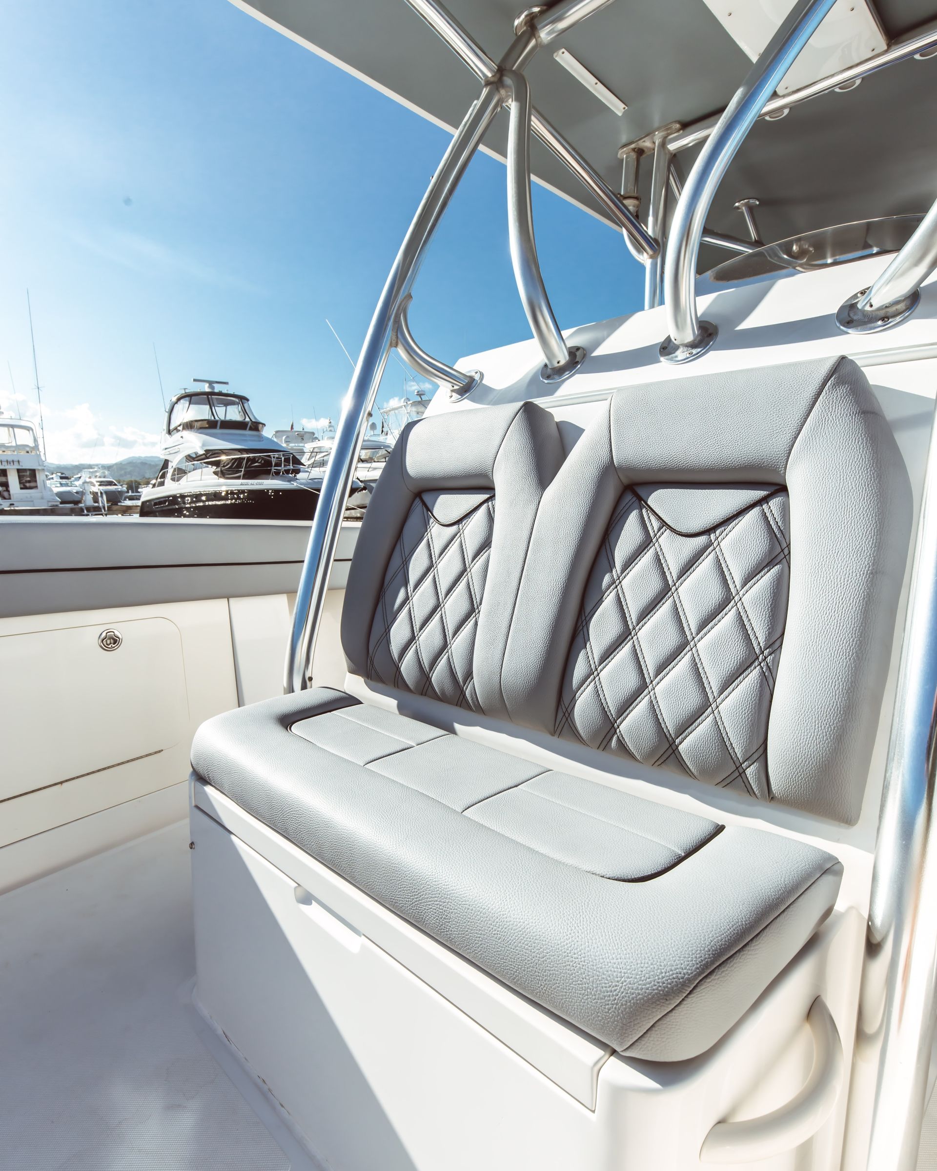 Gray cushioned bench seat on a boat with diamond-stitched backrests and a marina view in the background