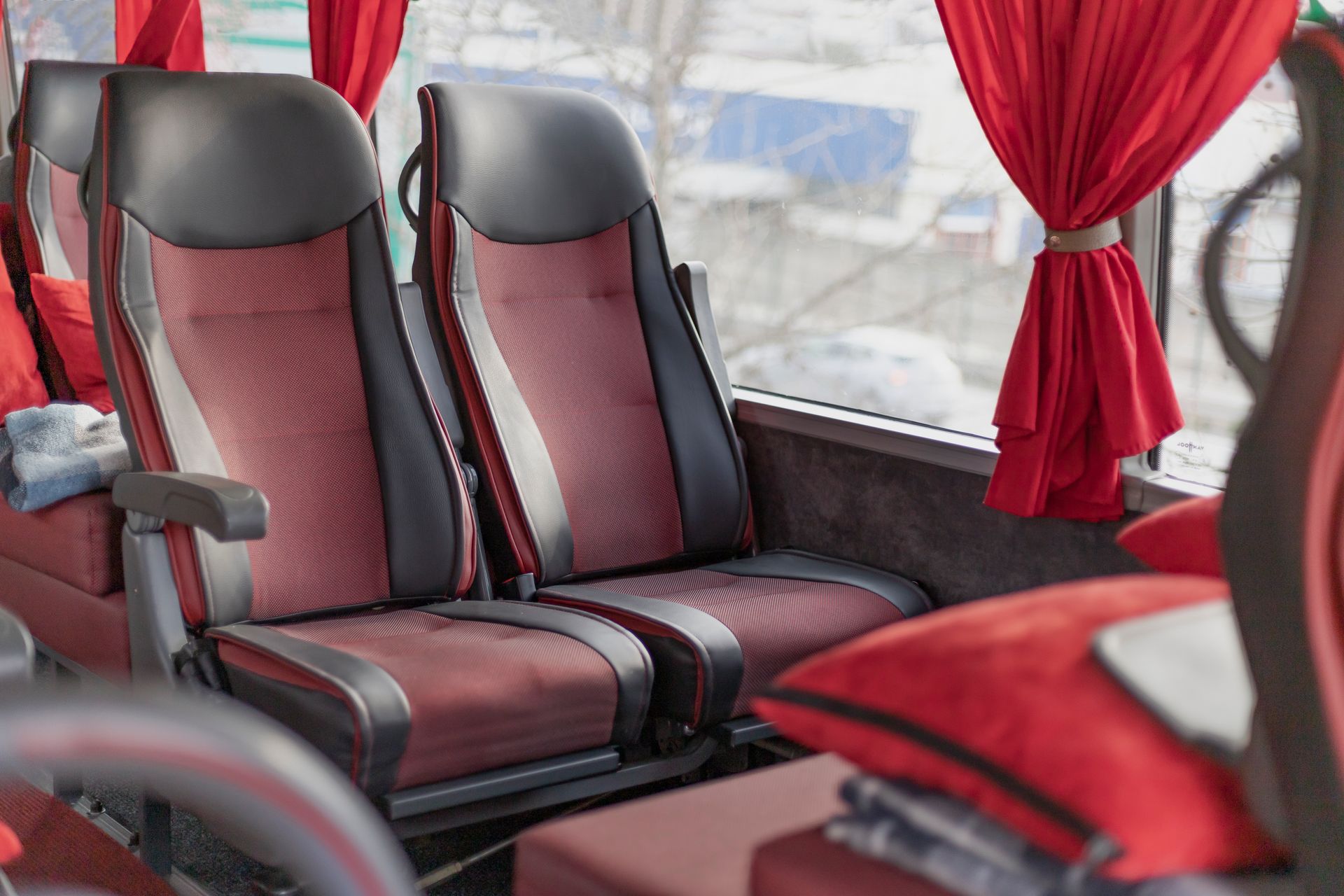 Red-and-black bus seats beside red curtains inside a coach bus