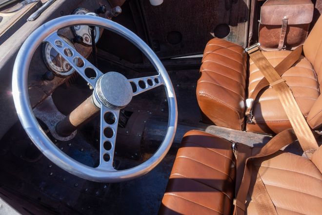 Vintage steering wheel among brown leather car seats in a cluttered storage area