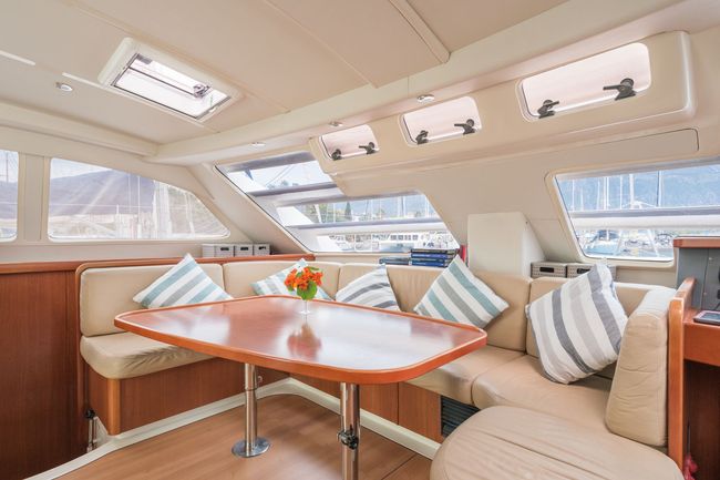 Bright yacht cabin with a wood table, beige seating, striped pillows, and large windows overlooking the water