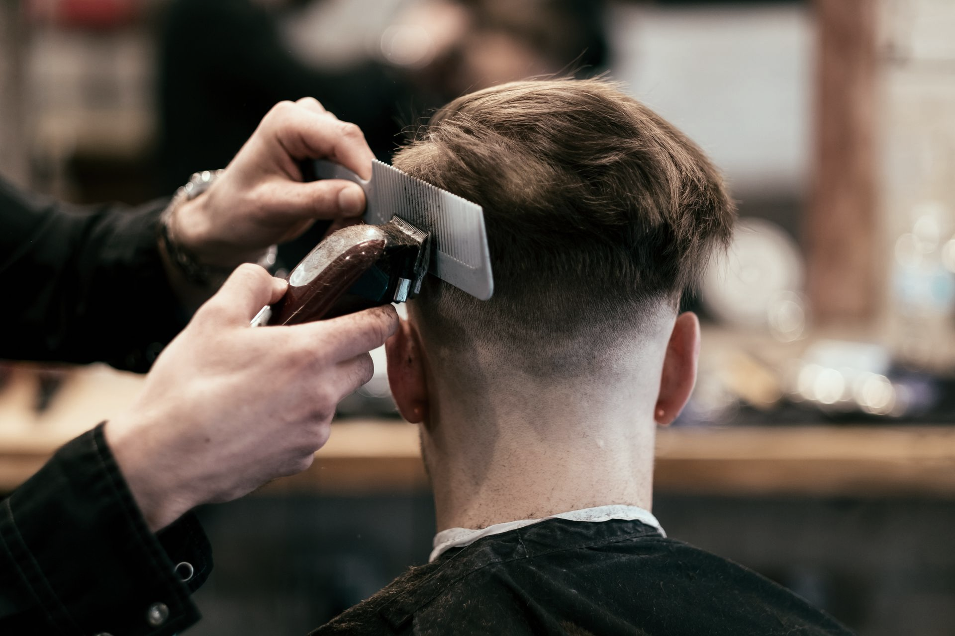 Un barbiere utilizza un tagliacapelli con protezione per tagliare i capelli di un cliente, creando una sfumatura.