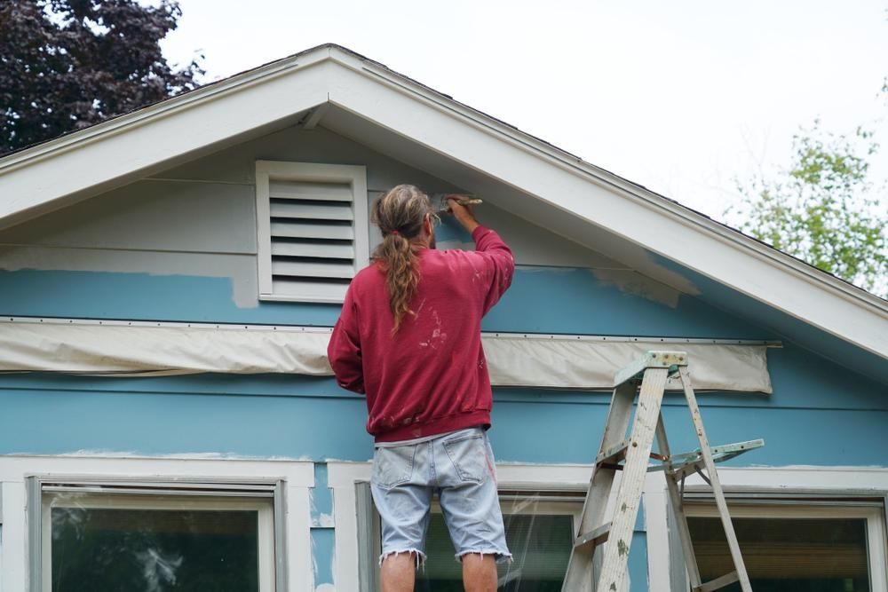A Man Is Standing On A Ladder Painting A Blue House — Strait Edge Painting In Gold Coast, NSW
