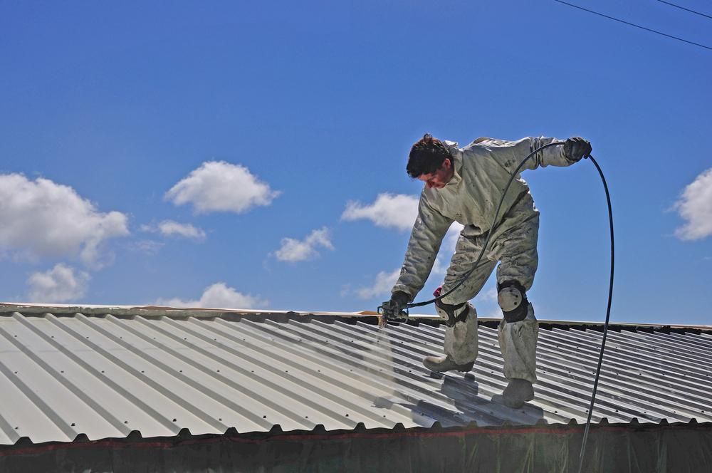 A Man Is Standing On Top Of A Metal Roof Spraying Paint — Strait Edge Painting In Tweed Heads South, NSW