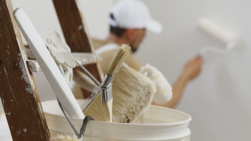 A Person in a White Hat and Overalls Uses a Paint Roller on a Wall — Strait Edge Painting In Byron Bay, NSW