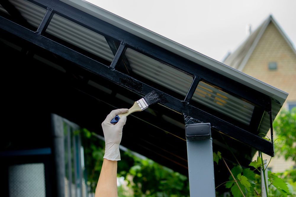 A Person Wearing a Glove Paints the Black Metal Frame of an Outdoor Roof — Strait Edge Painting In Tweed Heads South, NSW