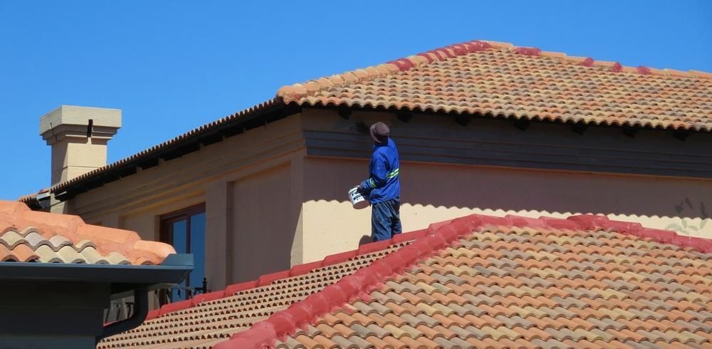 A Man Is Standing On Top Of A Tiled Roof And Painting On The Roof — Strait Edge Painting In Gold Coast, NSW