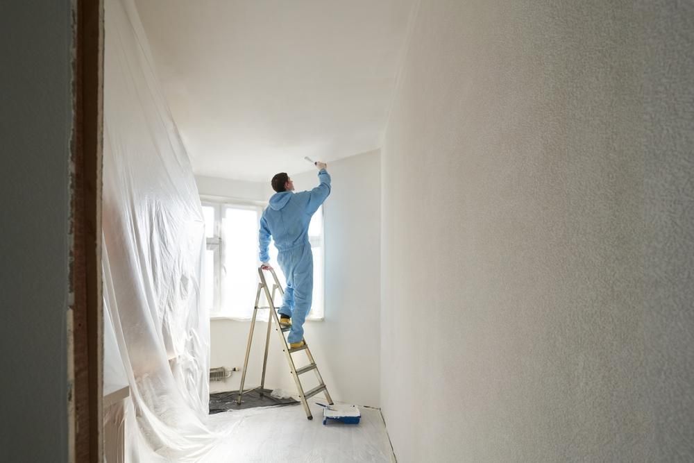 A Man Is Standing On A Ladder Painting A Wall — Strait Edge Painting In Tweed Heads, NSW