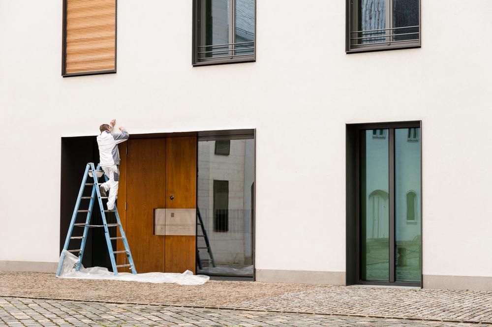 A Man Is Standing On A Ladder Painting A Building — Strait Edge Painting In Tweed Heads South, NSW