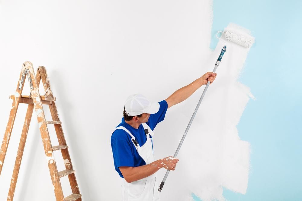 A Man Is Painting A Wall With A Paint Roller — Strait Edge Painting In Tweed Heads, NSW