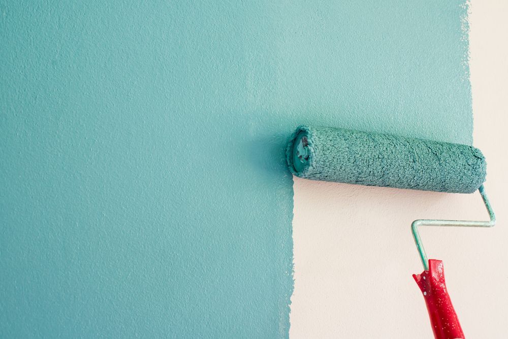 A Paint Roller is Applying Smooth Teal Paint to a Light Beige Wall — Strait Edge Painting In Byron Bay, NSW