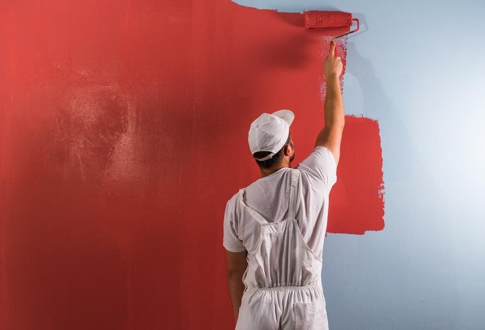 A Man Is Painting A Wall Red With A Paint Roller — Strait Edge Painting In Tweed Heads South, NSW