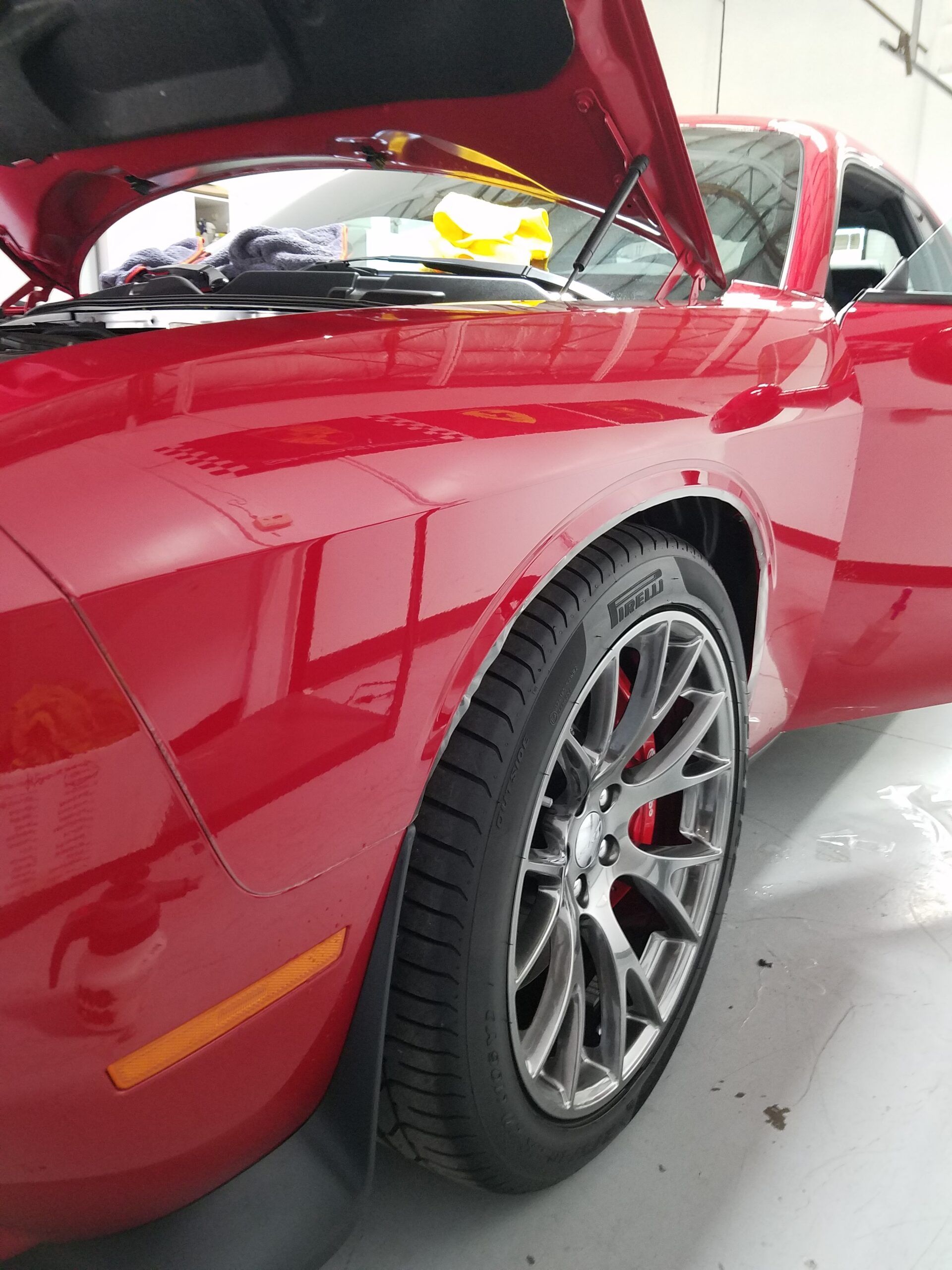Red sports car with hood open in a garage, showing the front wheel and engine bay.