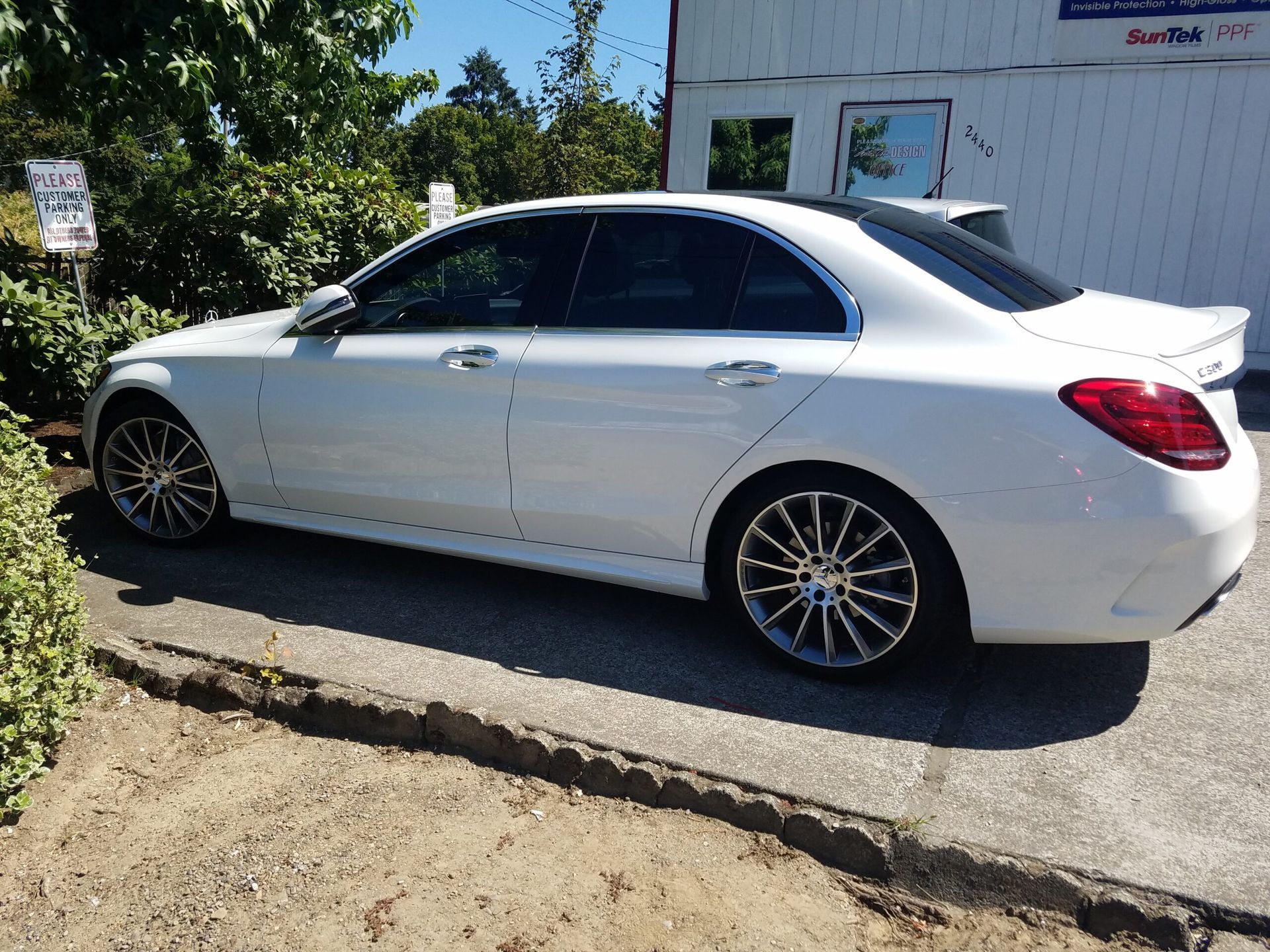 White sedan parked on a curb beside a building, viewed from the side.