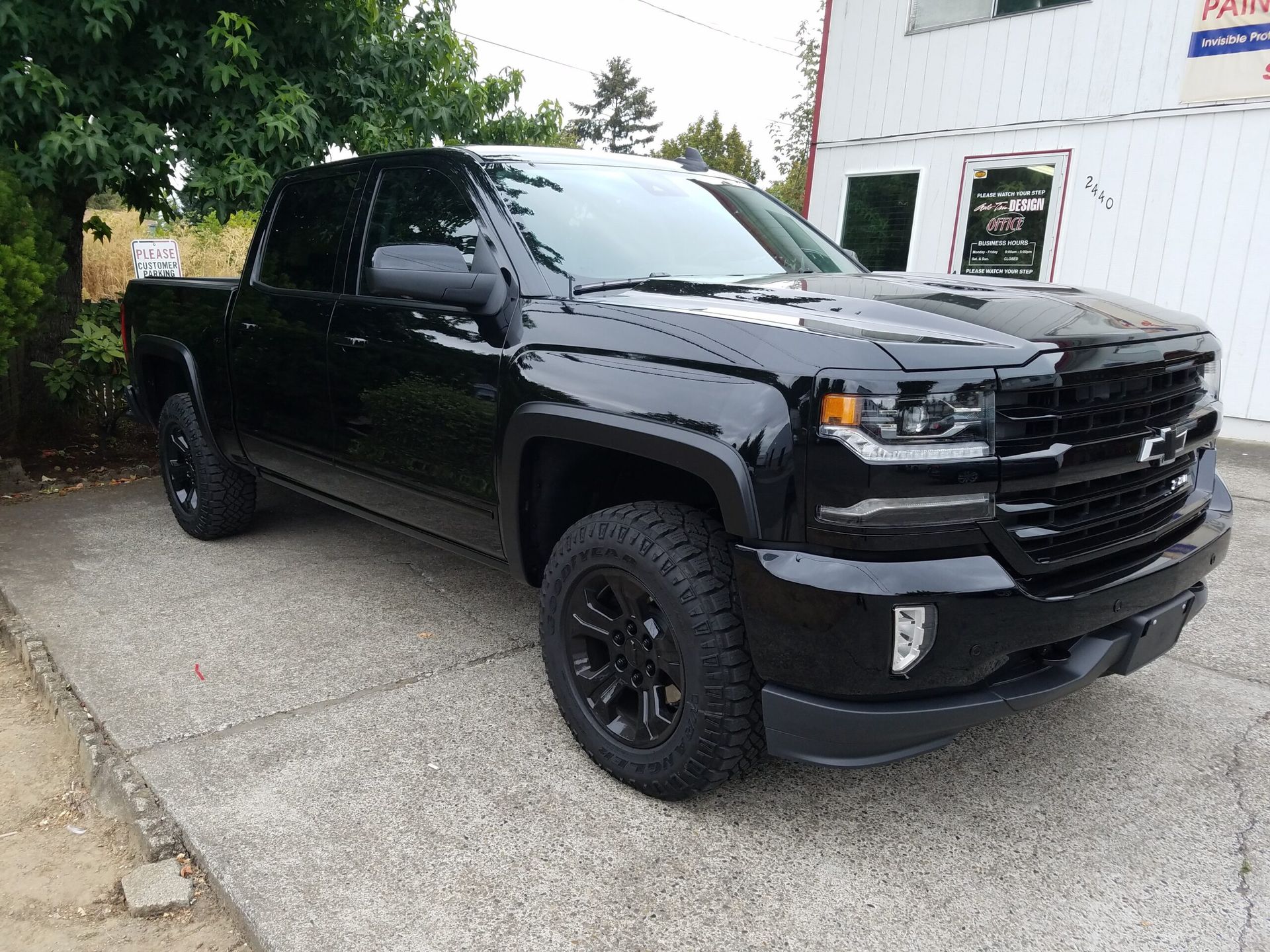 Black pickup truck parked on a driveway beside a white building