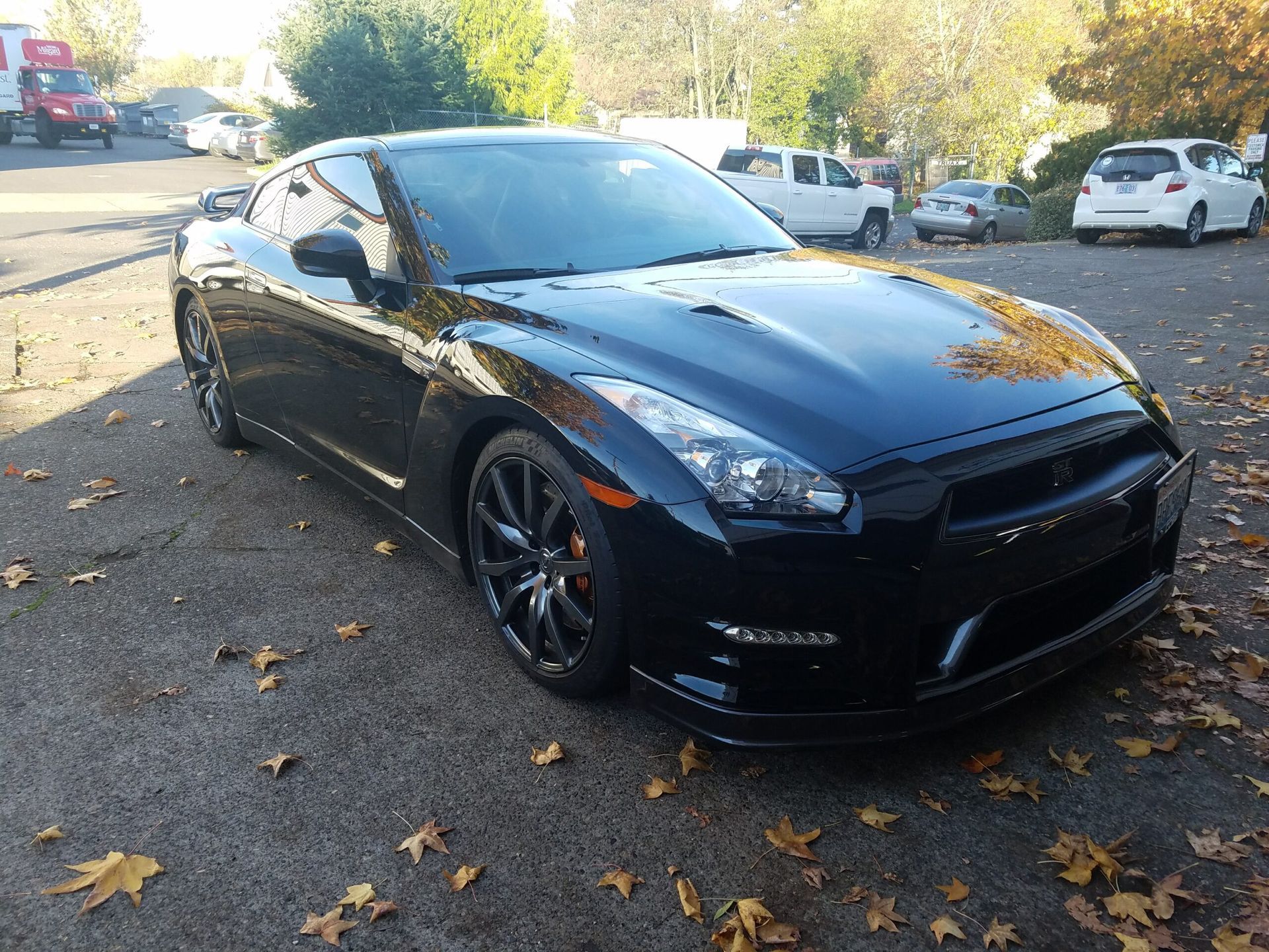 Black sports coupe parked on a leaf-strewn street in daylight, front-left view