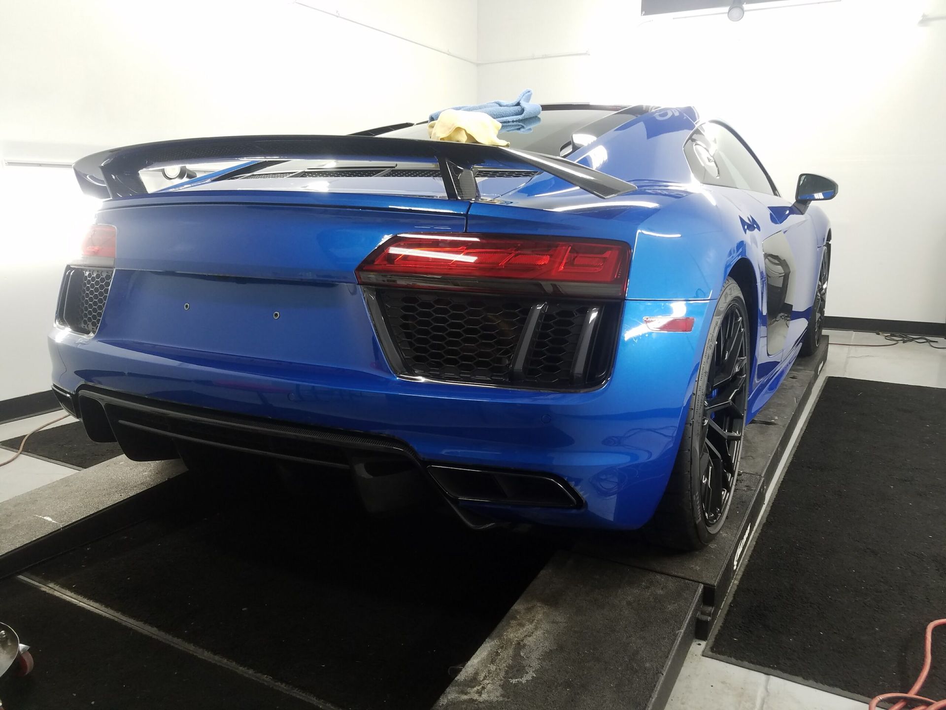 Blue sports car on a rolling road dynamometer in a garage, viewed from the rear.