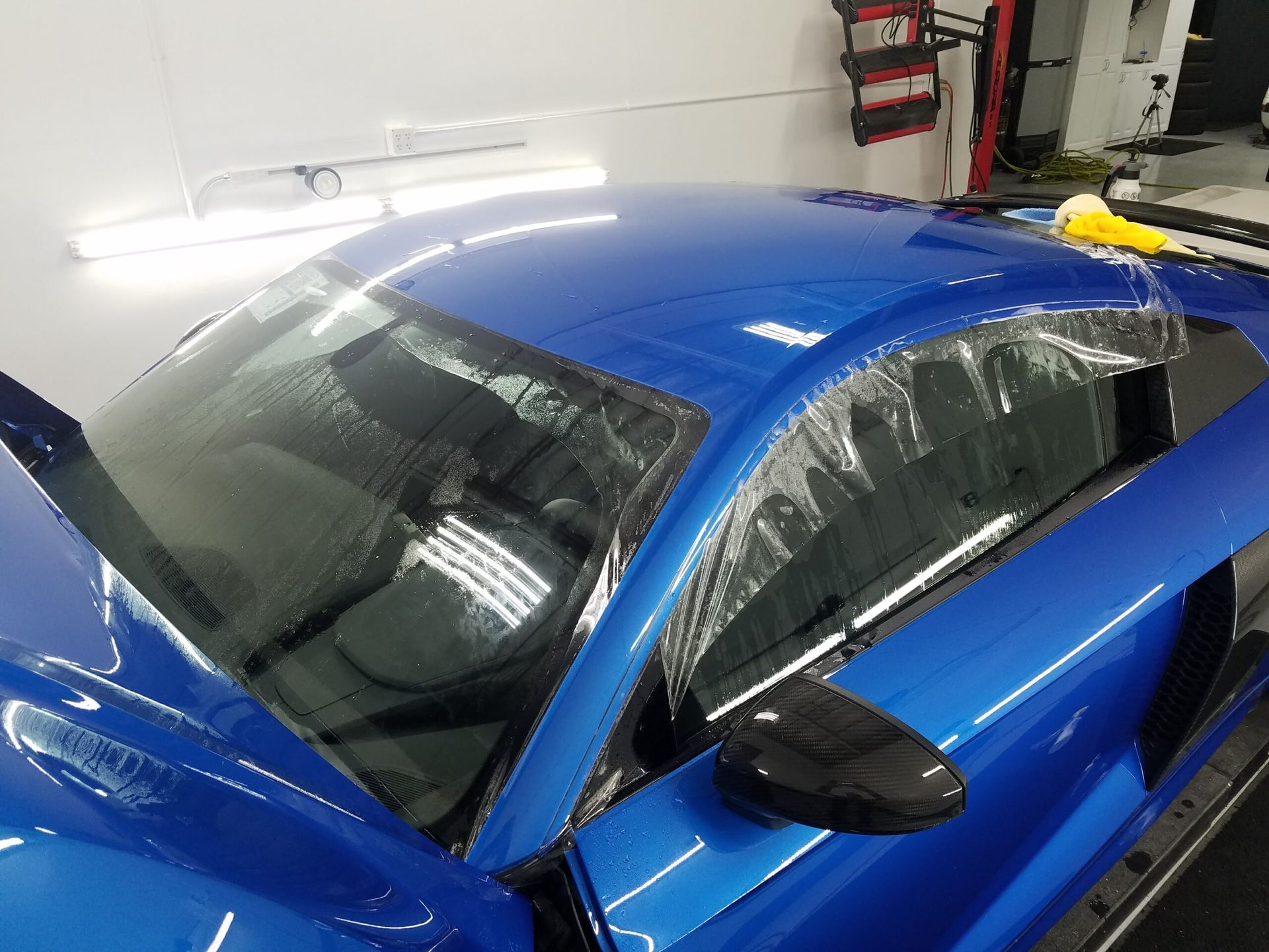 Blue sports car in a garage, seen from above with a glossy finish and rear side windows covered in plastic.