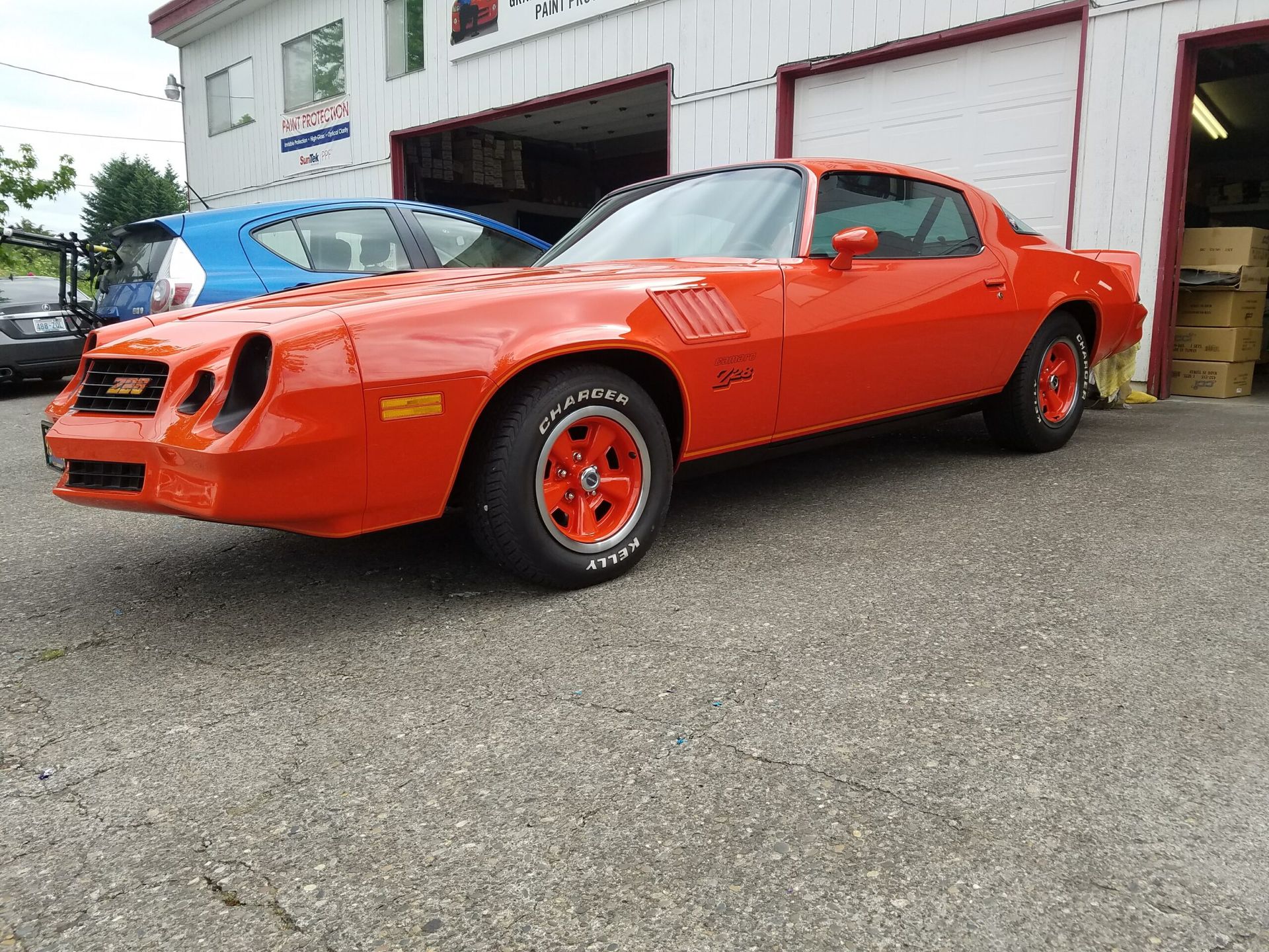 Bright orange classic sports car parked outside a garage on a paved driveway