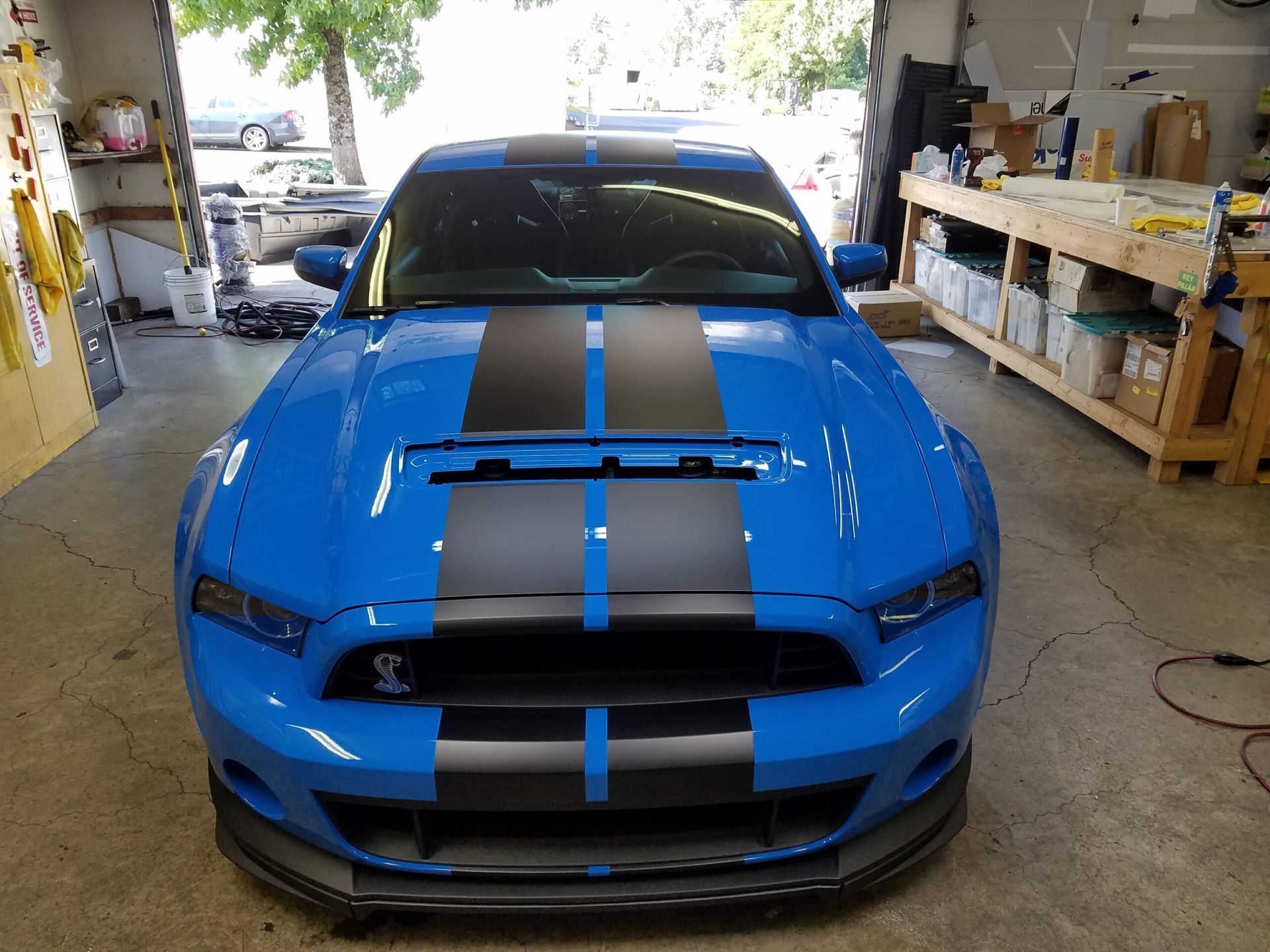 Blue sports car with black racing stripes parked inside a garage